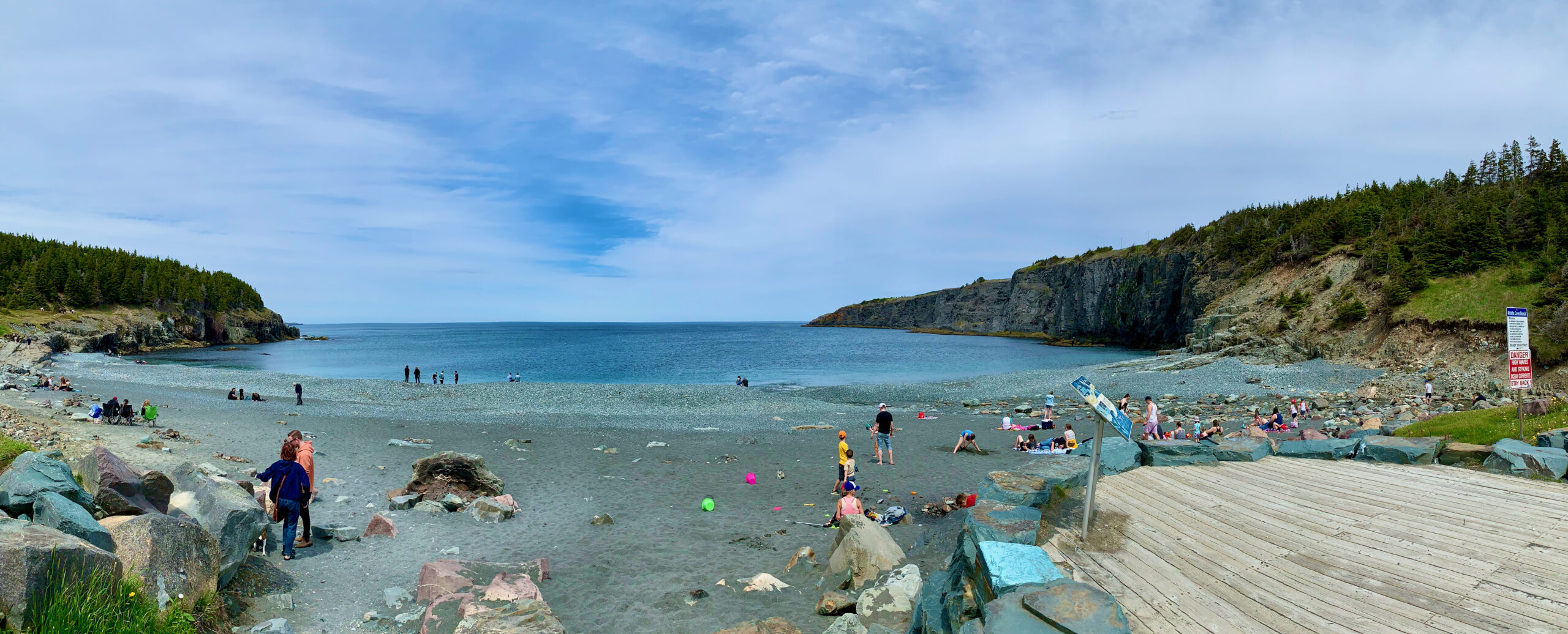 Panoramic view of a beach with a few families on it, with cliffs to the sides.