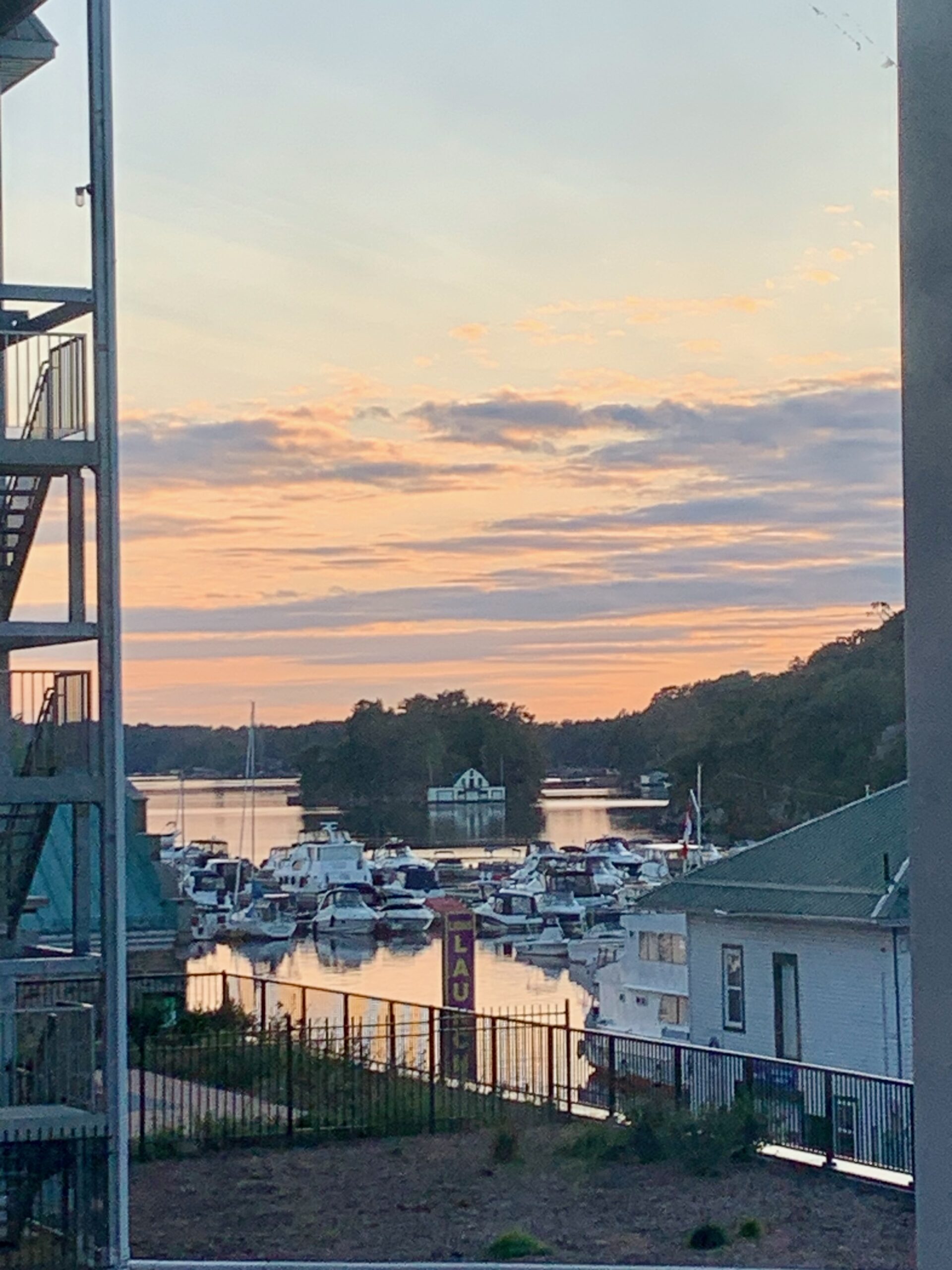 peaceful late day scene with boats in the foreground and glassy water with a picturesque cabin on an island under a colourful sky