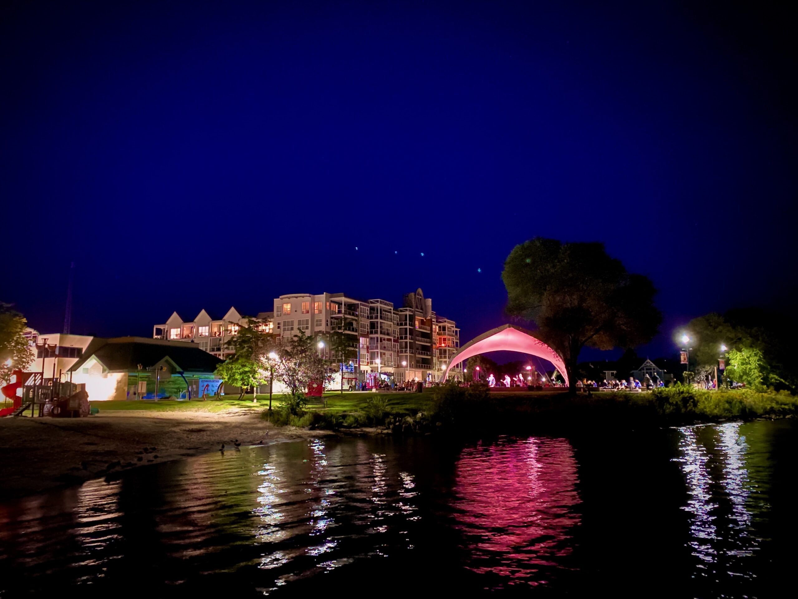 nighttime shot of a bandshell by a beach in a park with a four-storey building behind